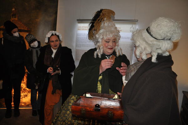 Zwei Damen im barocken Kostm sind in ein Gesprch vertieft. Im Hintergrund steht die Gstefhrerin im mittelalterlichen Kostm.