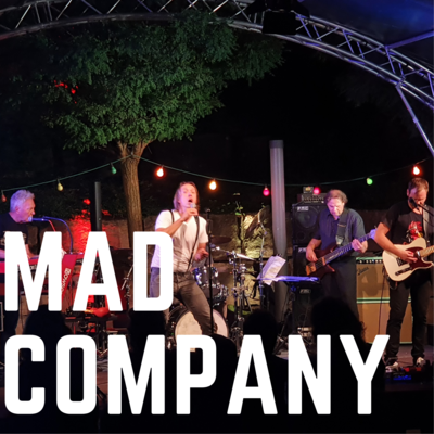 Bild vergrößern: Der Bandname "Mad Company" ist in weien Blockbuchstaben auf dem Foto zu sehen. Im Hintergrund ist die Musikgruppe Mad Company auf der Open-Air Bhne des Kultursommer 2021 zu sehen.