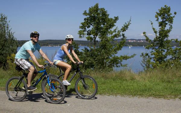 Zwei Radler fahren am See entlang.