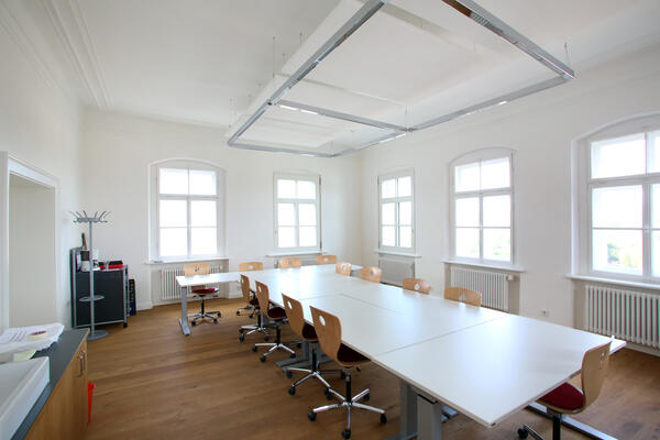Seminarraum der Volkshochschule.
Ein länglicher weißer Tisch mit braunen Stühlen.