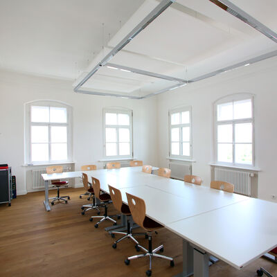 Bild vergrößern: Seminarraum der Volkshochschule.
Ein länglicher weißer Tisch mit braunen Stühlen.