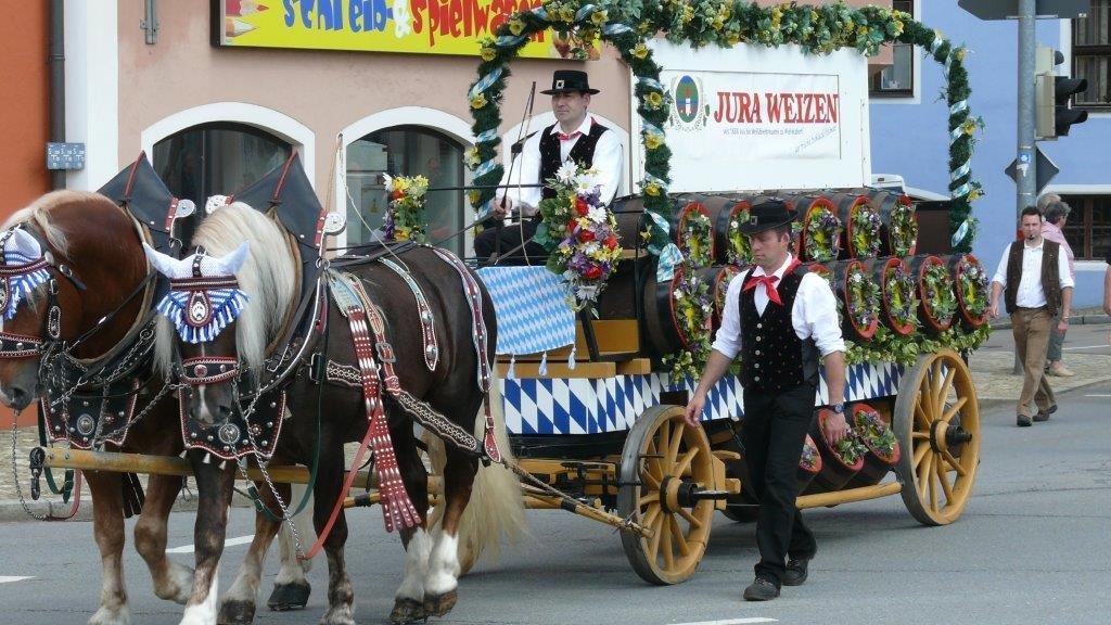 Bild vergrößern: Zei prachtvoll geschmückte Pferde ziehen den Wagen einer Brauerei, der auch geschmückt ist.