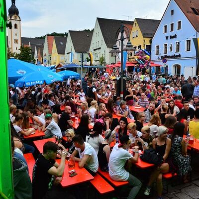 Bild vergrößern: Foto einer Menschenmenge auf dem Marktplatz beim Bürgerfest 2015. Menschen sitzen auf roten Bierbänken.
