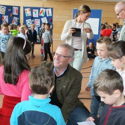 Bild vergrößern: Oberbürgermeister Andreas Feller kniend im Gespräch mit mehreren Erstklässlern. Im Hintergrund viele Schüler, eine Lehrerin und ein Reporter einer lokalen Tageszeitung.