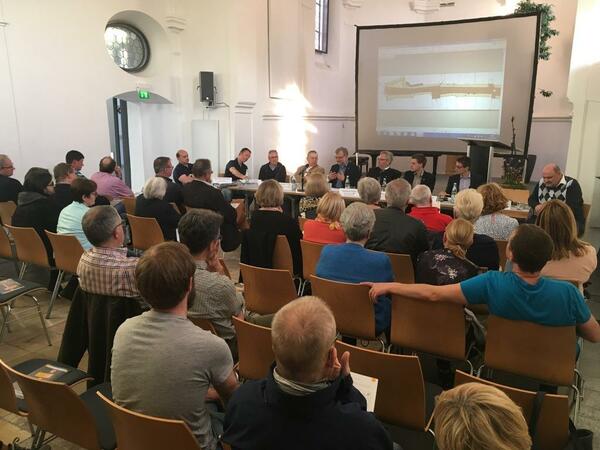 Bild vergrößern: Mehrere Menschen in einem Raum, vor einer Leinwand auf der eine Präsentation gezeigt wird.
