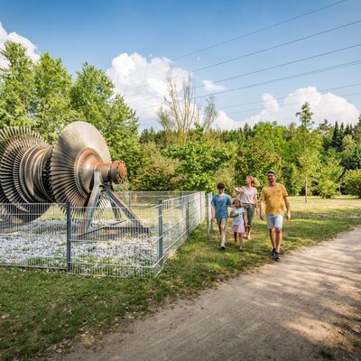 Bild vergrößern: Eine Familie geht vor einem Relik des Braunkohleabbaus spazieren.