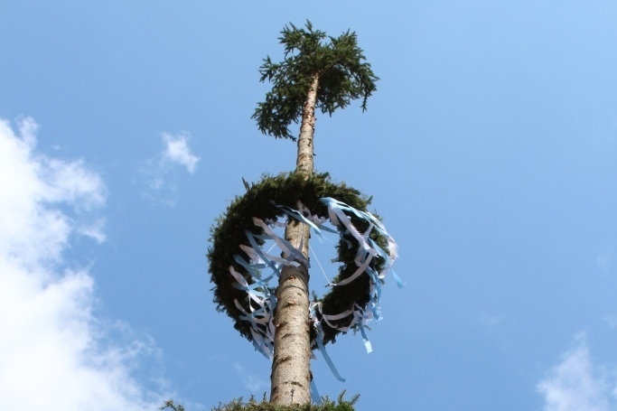 Bild vergr&ouml;&szlig;ern: Es zeigt einen Kirwabaum.
Ein Holzstamm an dem der Ringe aus Gr&uuml;nzeug h&auml;ngen.