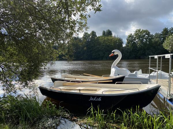 Zwei Ruderboote und ein Tretboot liegen an der Naab bereit.