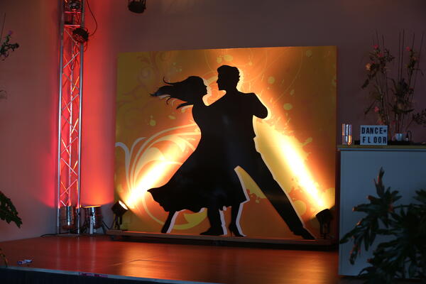 Bild vergrößern: Foto vom Logo des Stadtballs. Logo: Eine Frau und ein Mann tanzen. Die Figuren sind komplett in schwarz auf einem gelben Hintergrund. Es wird angeleuchtet.
