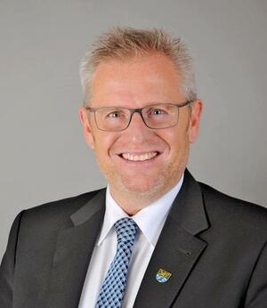 Das Bild zeigt ein Foto von Andreas Feller. 
Andreas Feller trägt eine Brille und hat einen dunklen Anzug an.
Und er trägt eine blaue Krawatte.