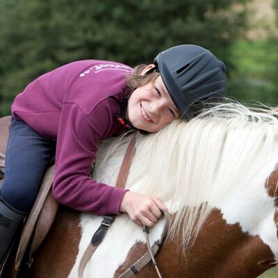 Bild vergrößern: Ein Mädchen liegt glücklich am Pferderücken.