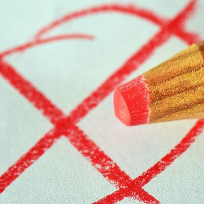 Roter Buntstift im Vordergrund, gezeichnetes, rotes Kreuz und Kreis im Hintergrund.