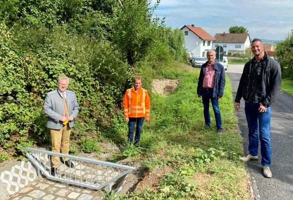 Bild vergrößern: Vier Personen vor einem Schutzgitter, das Überflutungen vermeiden soll.
