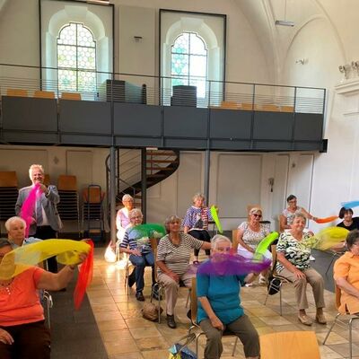 Bild vergrößern: Mehrere Senioren auf Stühlen in einer ehemaligen Kirche, im Hintergrund die Empore.