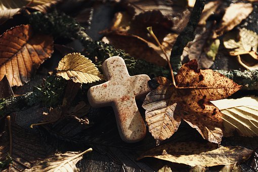 Kreuz auf Boden mit Blättern.
