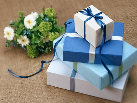 Geschenkpckchen mit blauem Geschenkpapier eingepackt und ein kleiner Blumenstrau mit weien und blauen Blumen.