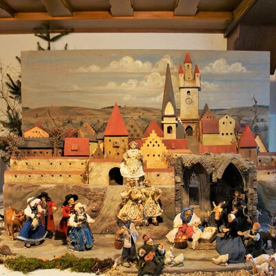 Bild vergrößern: Die Straubinger Krippe: Verbindung von Gäu und Wald zeigt 10 verschiedene Figuren, die sich auf dem Vorplatz des Burggrabens und unter einem halben Haus tummeln. Die Figuren auf dem Vorplatz tragen prächtige Kleidung. Die Figuren in dem halben Haus sehen dahingegen eher ärmlich aus.
