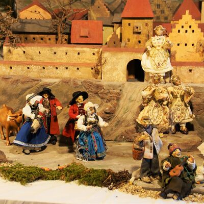 Bild vergrößern: Die Straubinger Krippe: Verbindung von Gäu und Wald zeigt 10 verschiedene Figuren, die sich auf dem Vorplatz des Burggrabens und unter einem halben Haus tummeln. Die Figuren auf dem Vorplatz tragen prächtige Kleidung. Die Figuren in dem halben Haus sehen dahingegen eher ärmlich aus.
