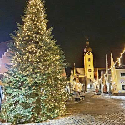 Mit Lichtern geschmckter Weihnachtsbaum. Am Abend beleuchtet. Auf dem Schwandorfer Marktplatz. Im Hintergrund der Kirchturm der Pfarrkirche Sankt Jakob.