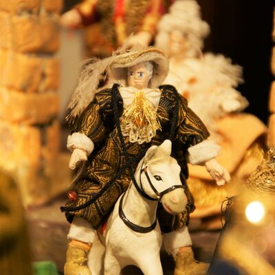 Bild vergrößern: Eine Figur der Krippe "Fünf Epiphanien als barockes Welttheater". Es ist ein Reiter auf einem weißen Pferd. Die Figur trägt ein prachtvolles braunes Gewand und einen hellbraunen Hut.