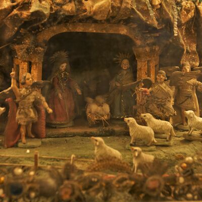 Bild vergrößern: Figuren aus der "Rokoko Kastenkrippe". Es zeigt den Wald und eine Höhle in der die heilige Familie beisammen ist. Vor der Höhle stehen Engeln und Schafe.
