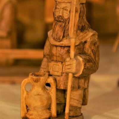 Bild vergrößern: Eine aus Holz geschnitze ältere Figur mit langem Bart und Stab in der Hand. Grimmiger Gesichtsausdruck. Vor der Figur steht auf dem Boden ein Gefäß.