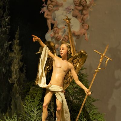 Bild vergrößern: Bei der Krippe "Hirtenverkündigung" zeigt ein Engel in den Himmel. Die Flügel und das Kreuz in seiner Hand sind aus Gold.