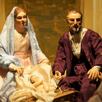 Bild vergrößern: Die Weihnachtskrippe der Familie Pöllmann. Zwei frauliche Figuren und zwei männliche Figuren, in der Mitte hell beleuchtet das Jesu-Kind.