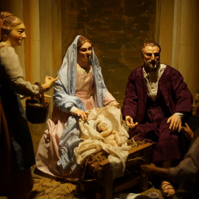 Bild vergrößern: Die Weihnachtskrippe der Familie Pöllmann. Zwei frauliche Figuren und zwei männliche Figuren, in der Mitte hell beleuchtet das Jesu-Kind.