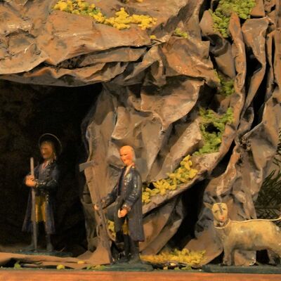 Bild vergrößern: Detailaufnahme des rechten Höhleneinganges. Im Hintergrund ist Josef in der Höhle zu sehen, mit Stab in der Hand. Im Vordergrund ist ein gut gekleideter älterer Mann abgebeildet, sowie eine Ziege.