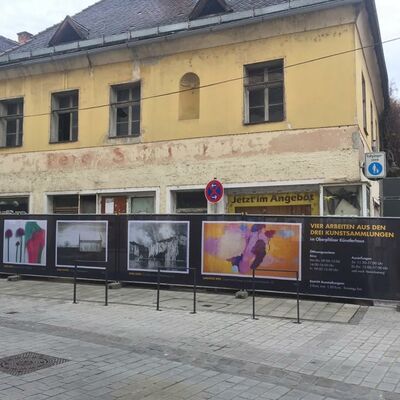 Bild vergrößern: Banner mit vier Bildern vor einer Häuserfassade in der Innenstadt.