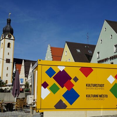 Bild vergrößern: Gelber Container mit den vielen verschiedenfarbigen Vierecken, die das Logo des Kulturstadtjahres zieren. Der Container ist teils aus Metall, teils aus Glas und begehbar.