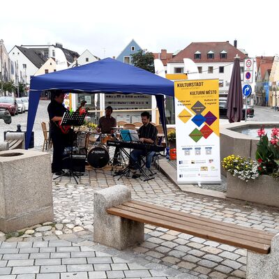 Bild vergrößern: Eine dreiköpfige Band mit Schlagzeug, Keyboard und Gitarre am Marktplatz in Schwandorf unter einem Pavillon.