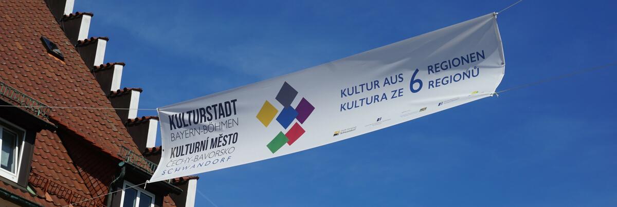 Bild vergrößern: Ein weißes Banner mit bunten Vierecken in der Mitte und einer großen Aufschrift der Kulturstadt Bayern-Böhmen in Schwandorf.