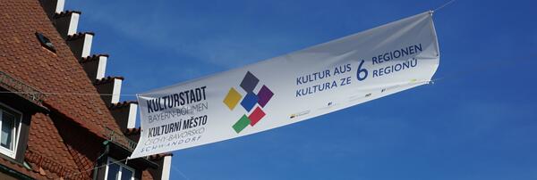 Ein wei&szlig;es Banner mit bunten Vierecken in der Mitte und einer gro&szlig;en Aufschrift der Kulturstadt Bayern-B&ouml;hmen in Schwandorf.
