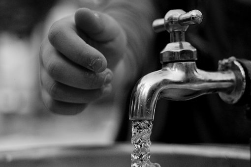 Trinkwasserhahn im Vordergrund und eine menschliche Hand im Hintergrund.