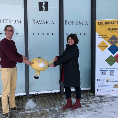 Bild vergrößern: Veronika Hofinger und David Bender halten das Kulturstadt-Maskottchen in der Hand. (Der Knödel)