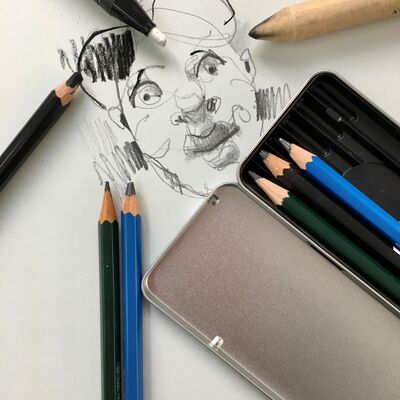Ein Blatt Papier auf das ein Gesicht gemalen ist und rundherum liegen verschiedene Stifte.