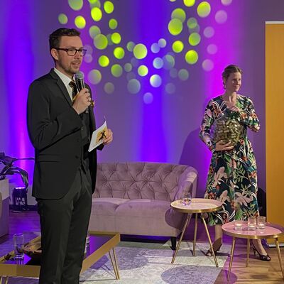 Foto: Die Stadtballmoderator:innen Johannes Lohrer und Anna Theuerl stehen in der Lounge mit einem Glas voller Korken in der Hand. Dies war an dem Abend eine Schätzfrage.