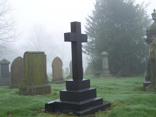 Bild vergrößern: Groes schwarzes Grabkreuz aus Stein im Vordergrund.