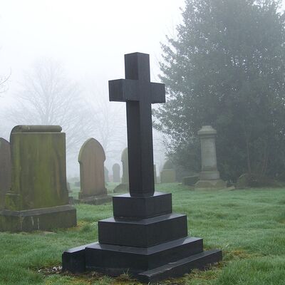 Gro&szlig;es schwarzes Grabkreuz aus Stein im Vordergrund.