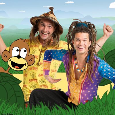 Bild vergrößern: Zwi Männer lachend in bunten Klamotten stehen vor einer animierten Dschungellandschaft.