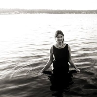 Bild vergrößern: Ein schwarz weiß Foto, dass eine Frau in einem dunklen Kleid in einem See zeigt.