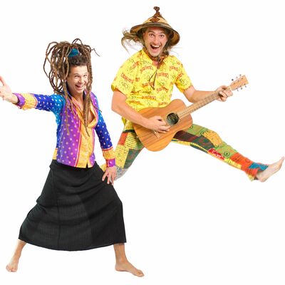Bild vergrößern: Zwei bunt gekleidete und tanzende Männer. Einer der beiden trägt einen Rock und Rasterzöpfe. Der andere Trägt einen Hut und hat eine Gitarre in der Hand
