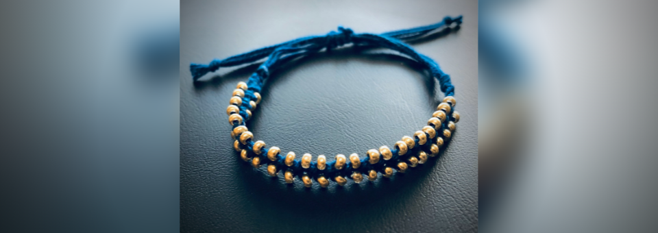 Bild vergrößern: Ein blaues Makramee-Armband mit goldenen Perlen.