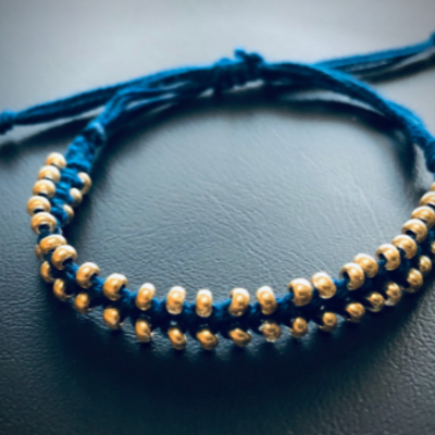 Ein blaues Makramee-Armband mit goldenen Perlen.