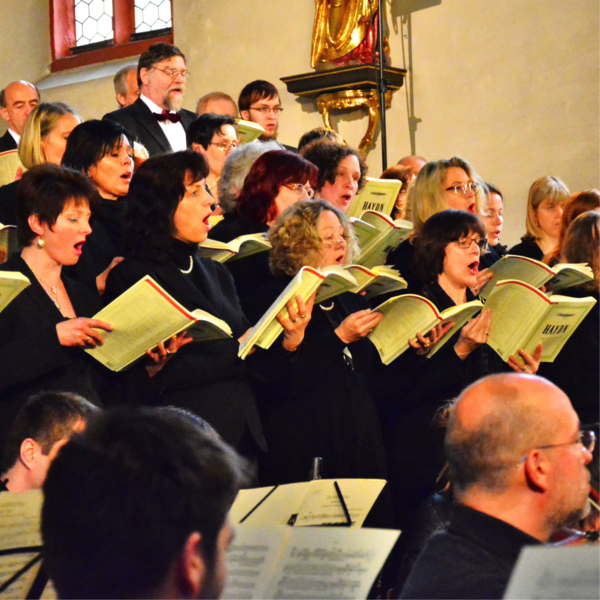 Chor. Viele Persone mit Gesangsbchern singen.