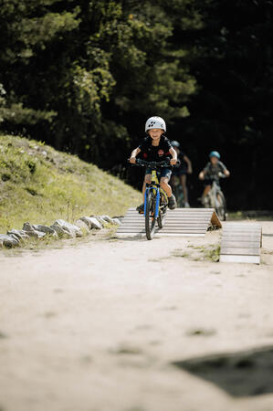 Bild vergrößern: Kinder fahren mit dem Rad über verschiedene Hindernisse aus Holz.