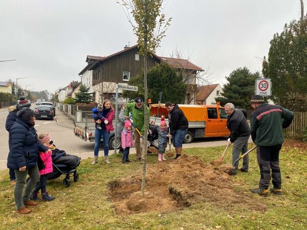 Mehrere Erwachsene und Kinder pflanzen einen Baum.