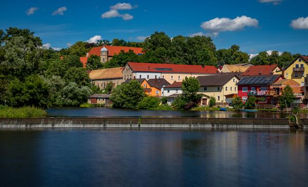 Blick auf Schloss Fronberg. Es sind noch weitere Häuser in bunten Farben und der Fluss Naab zu sehen.